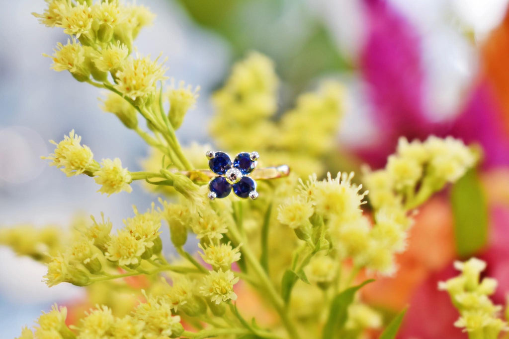 bague en forme de fleur avec quatre saphir posée sur des fleurs